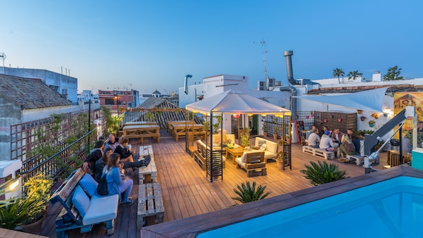 Un bar en la azotea con mobiliario de madera, una piscina y una zona de estar cubierta.
