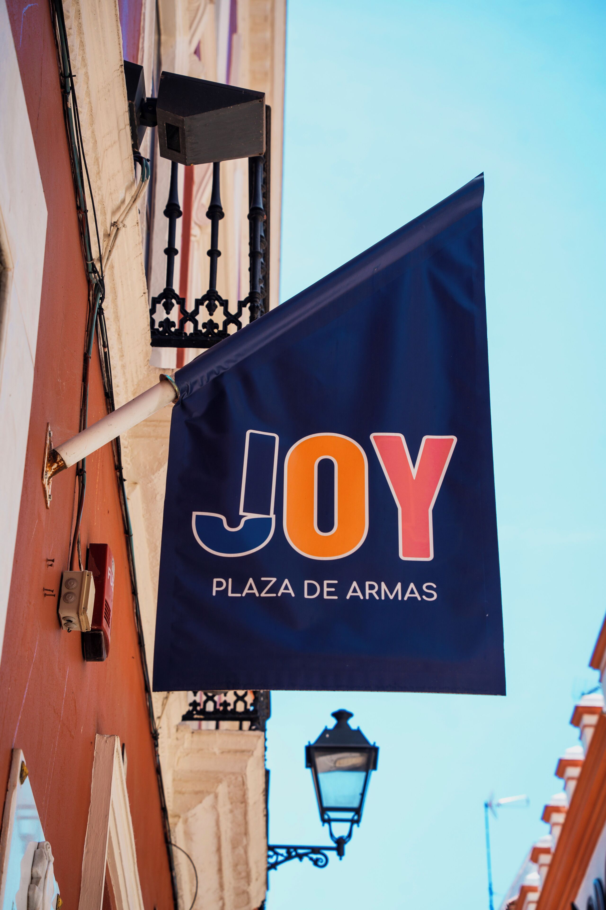 Een vlag met de tekst 'JOY PLAZA DE ARMAS' aan een gebouw bevestigd.