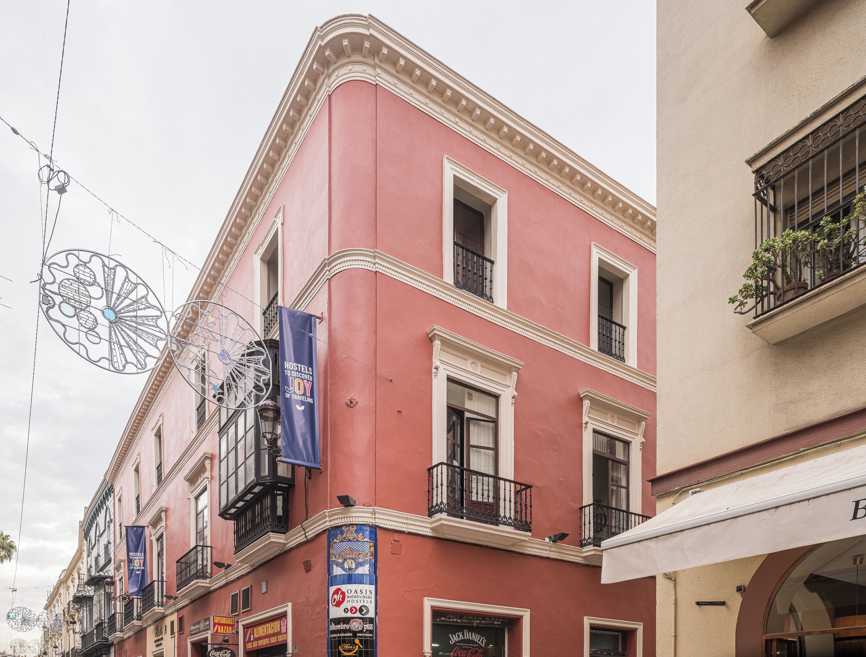 A pink building with multiple balconies, a sign for 'Jack Daniel's', and a 'Hostels to Discover Joy of Traveling' banner.