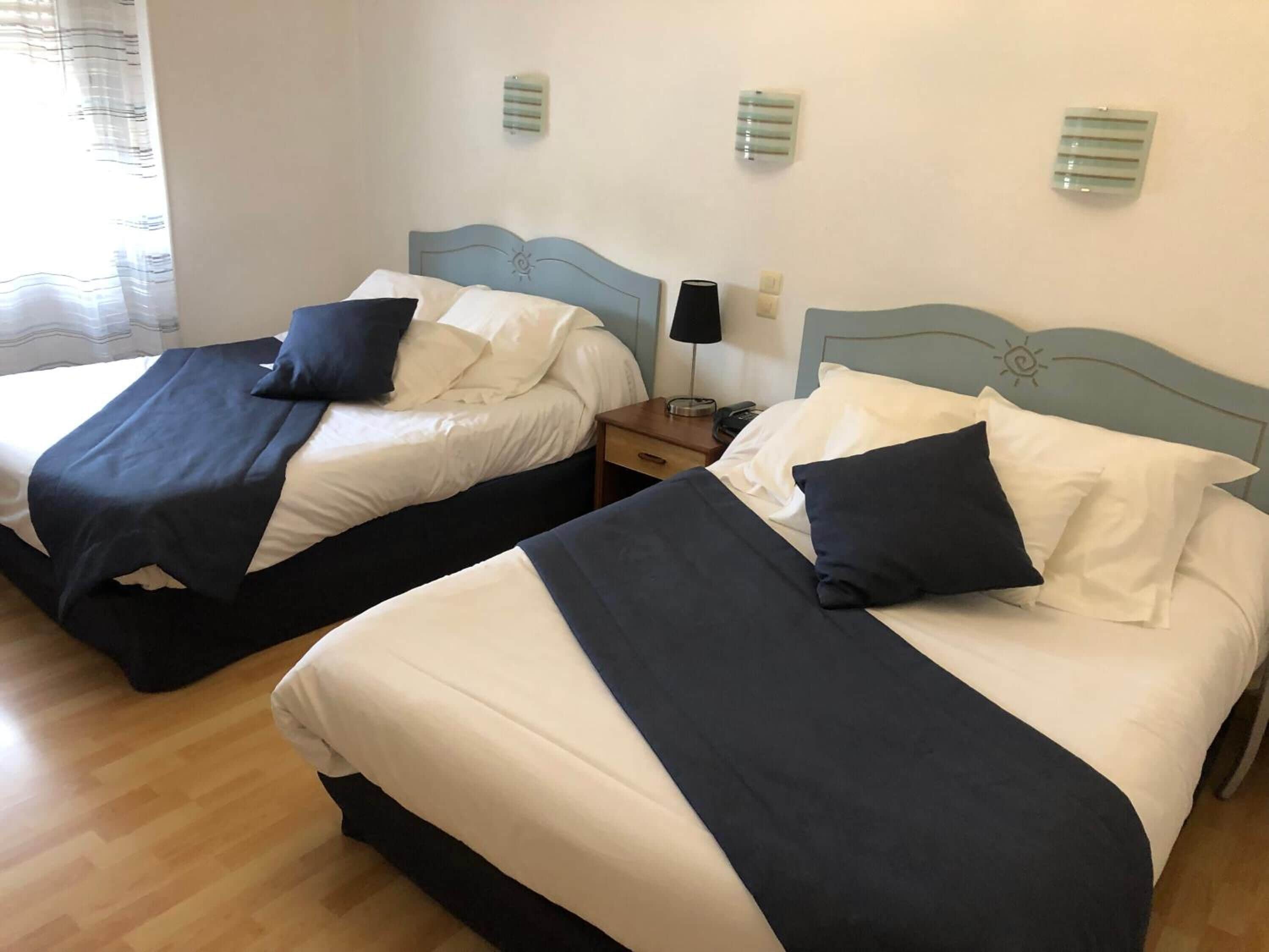 Zwei Einzelbetten mit passenden Kopfteilen, weiße Bettwäsche und dunkelblaue Zierkissen. An jedem Bett steht ein Nachttisch mit Lampe und Telefon.