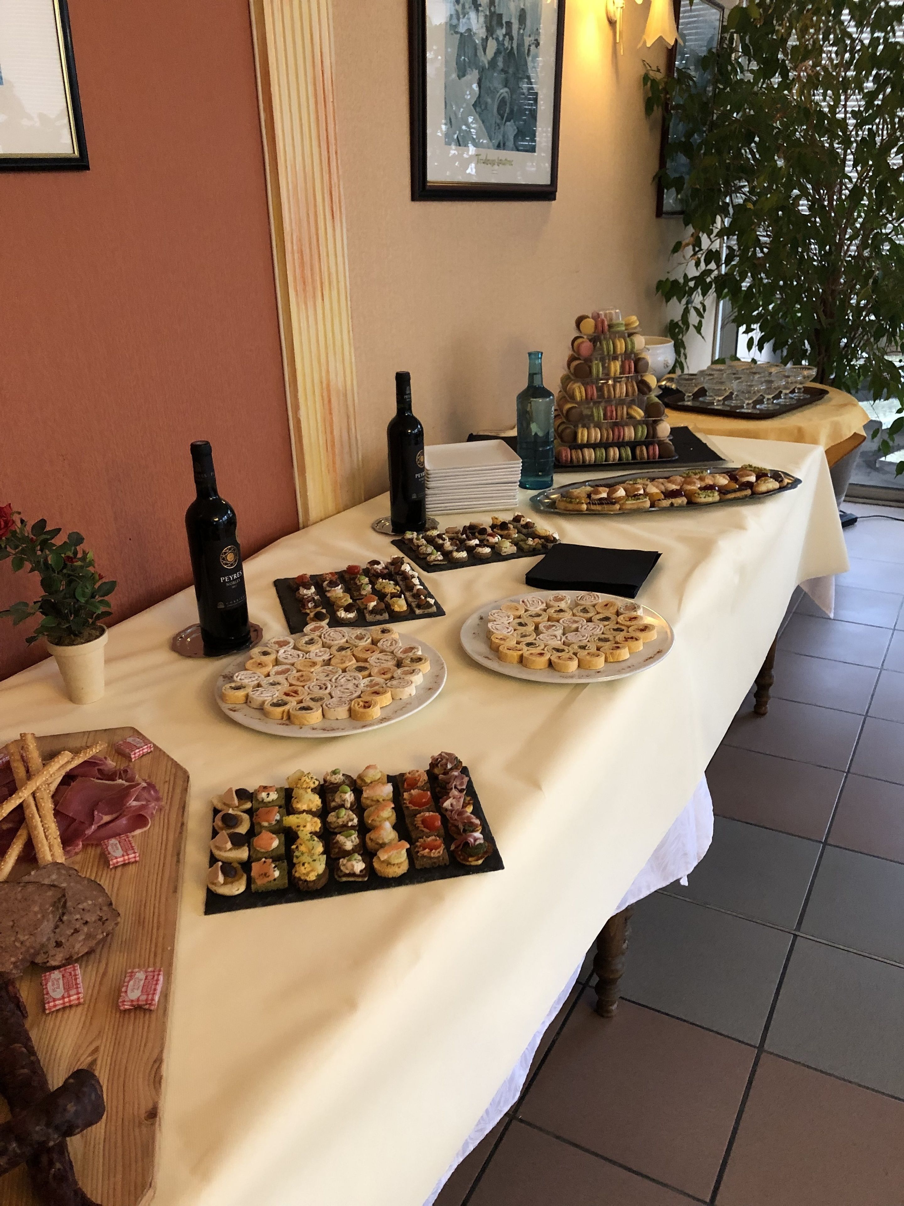 Une table de buffet proposant divers plats, notamment des pâtisseries, des macarons et un assortiment de vins.
