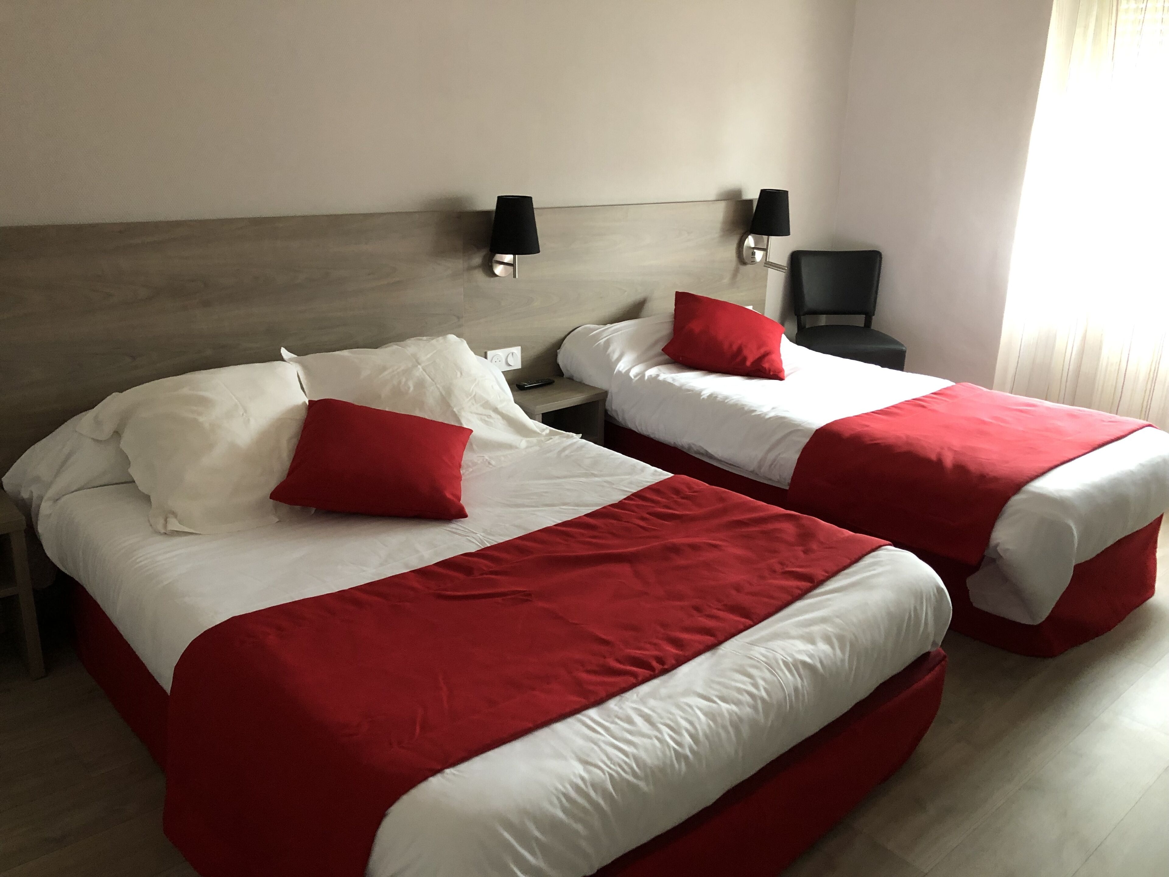 Hotelkamer met twee bedden, elk voorzien van rode en witte beddengoed, een houten hoofdbord en wandlampen.