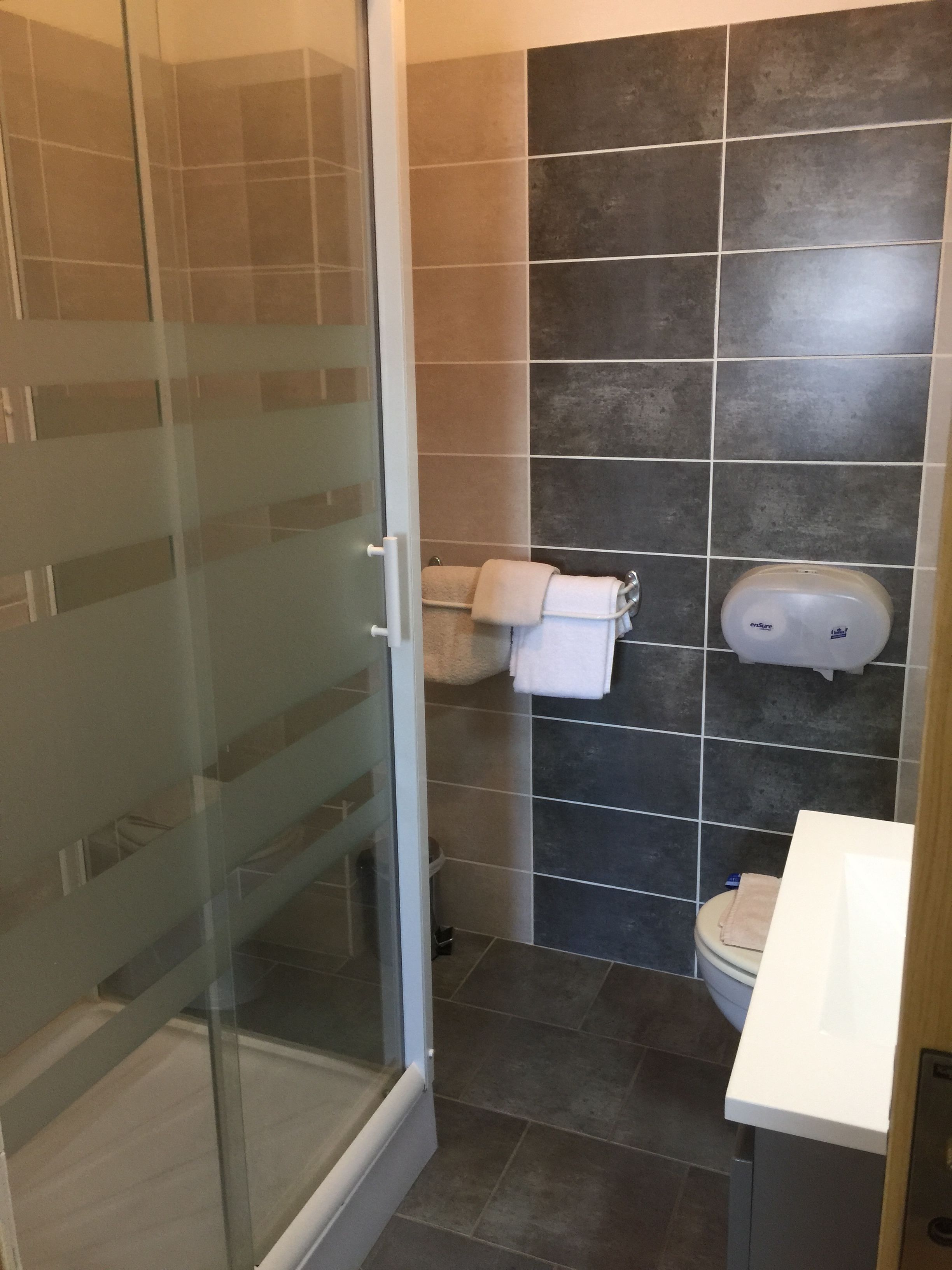 A bathroom with a glass shower door, a toilet, and a hand dryer.