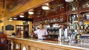 A bar area with a bartender, wooden bar counter, stools, and shelves stocked with bottles. - Le Roi Gourmand (Pamiers)