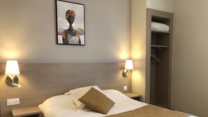 A hotel room with a bed, two bedside tables, a wall-mounted lamp, a coat closet, and a framed picture on the wall. - Le Roi Gourmand (Pamiers)