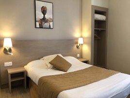 Habitación de hotel con cama, dos mesitas de noche, lámpara de pared, armario y un cuadro en la pared.