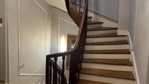 A staircase with wooden steps and a dark wooden handrail, leading to a landing with a chandelier. - Le Roi Gourmand (Pamiers)