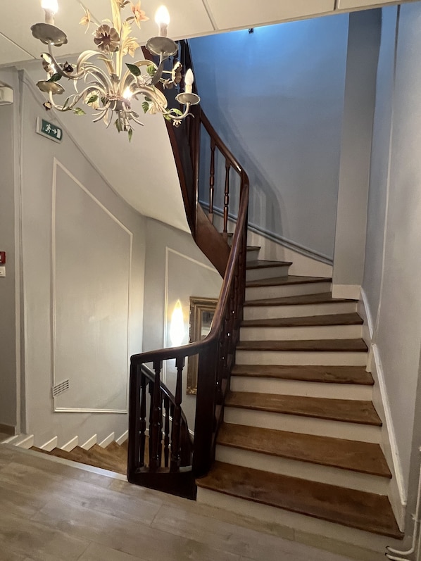 A staircase with wooden steps and a dark wooden handrail, leading to a landing with a chandelier.