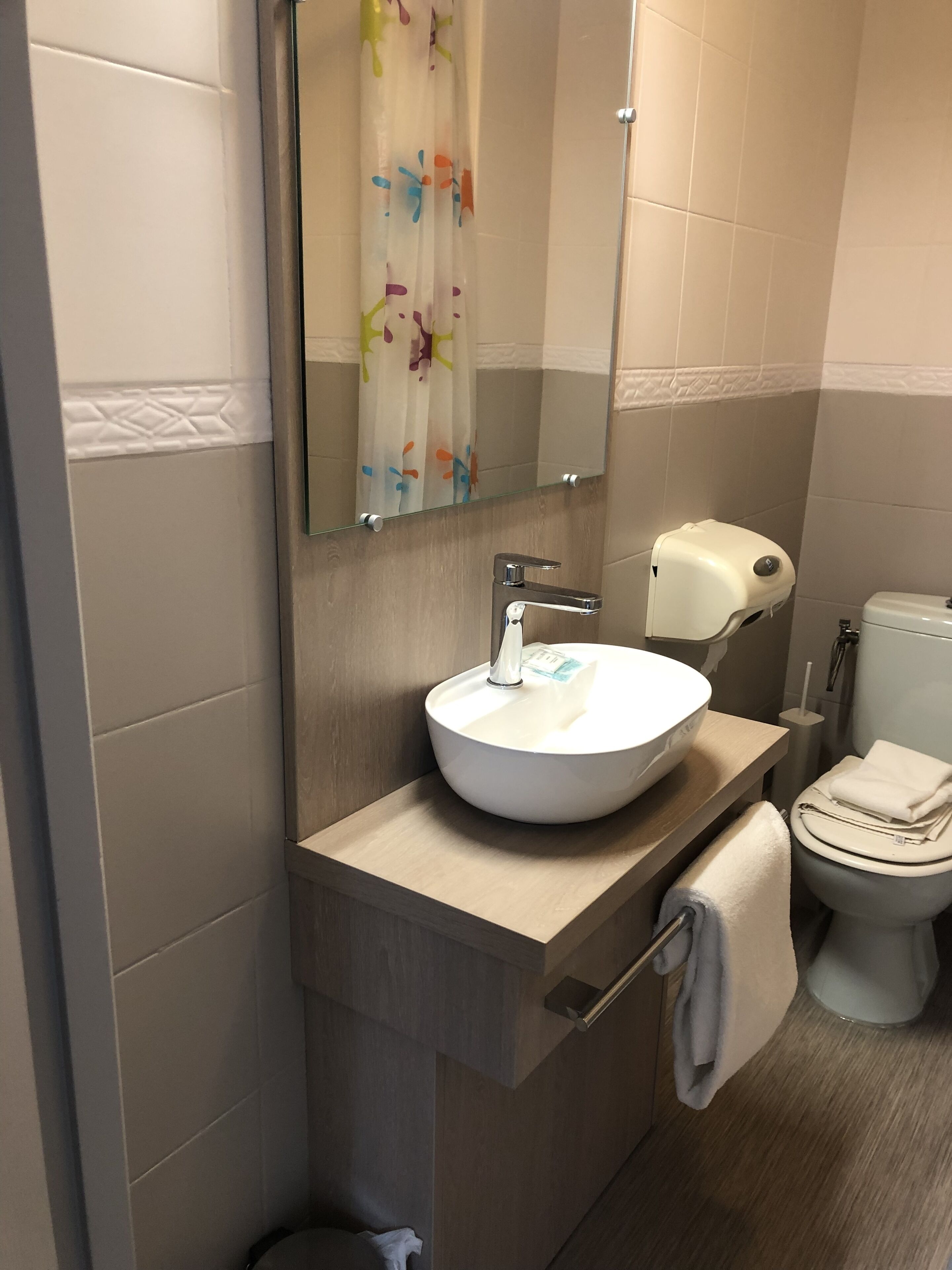 Un baño moderno con un lavamanos blanco, un espejo, un inodoro y un perchero para toallas.