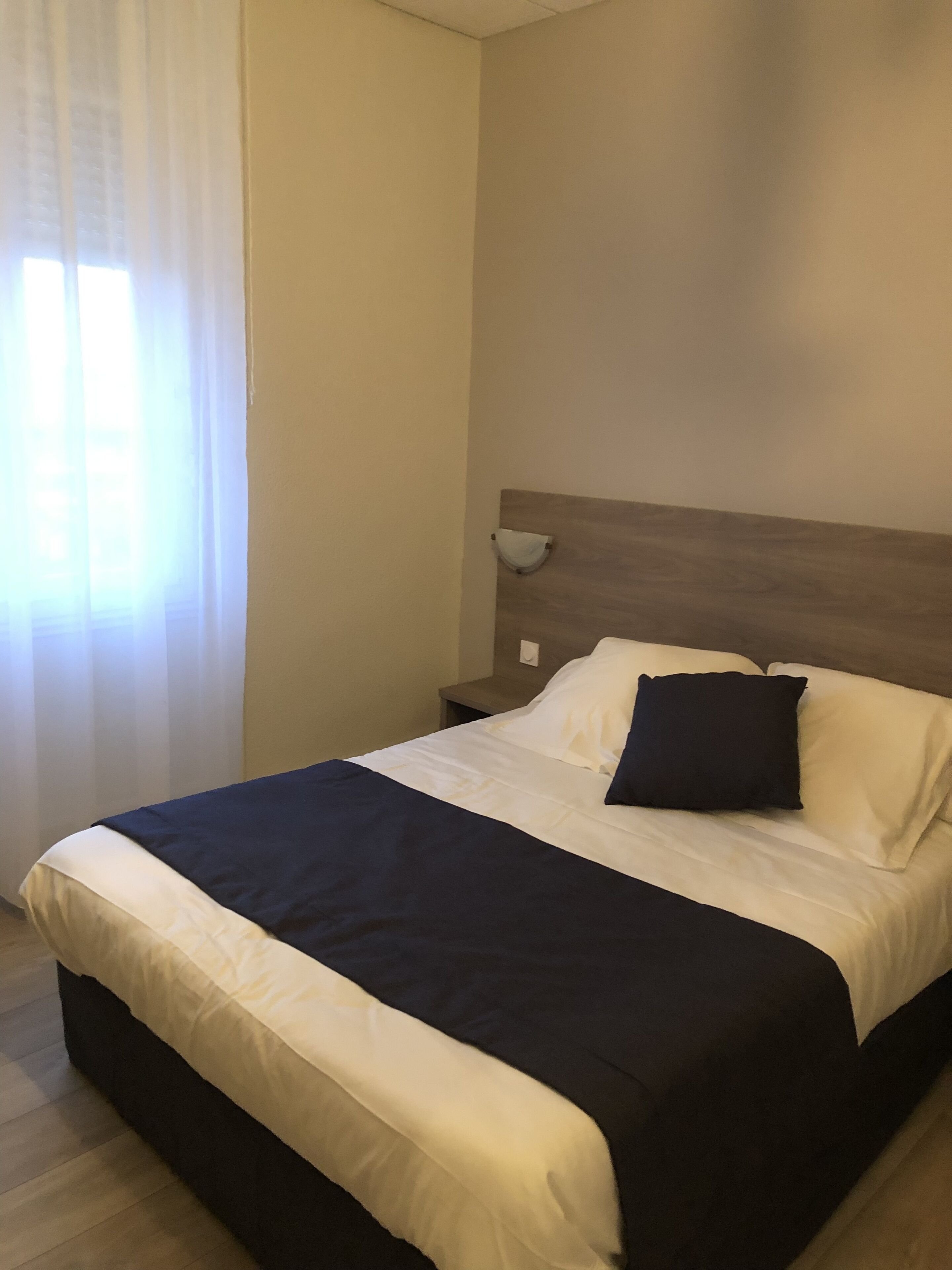 A neatly made bed with white and dark bedding, a wooden headboard, and a bedside table with a lamp.