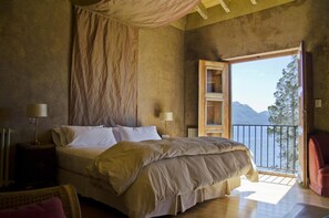 A bedroom with a large bed, a nightstand, a chair, and a view of a mountain through a balcony. - Luma Casa de Montana (Villa La Angostura)