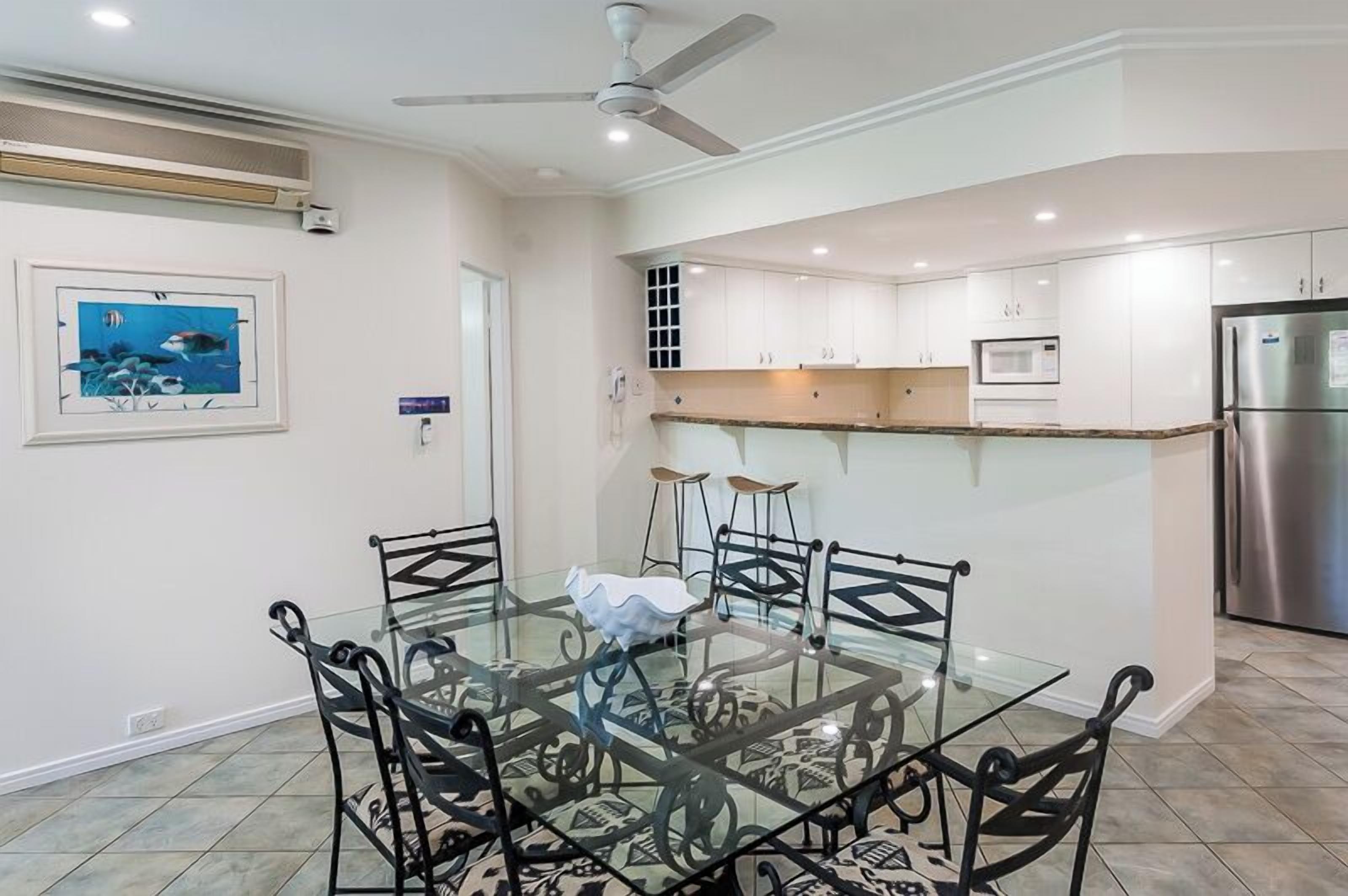 Una cocina moderna con armarios blancos, un refrigerador de acero inoxidable y una mesa de comedor de vidrio con sillas negras.