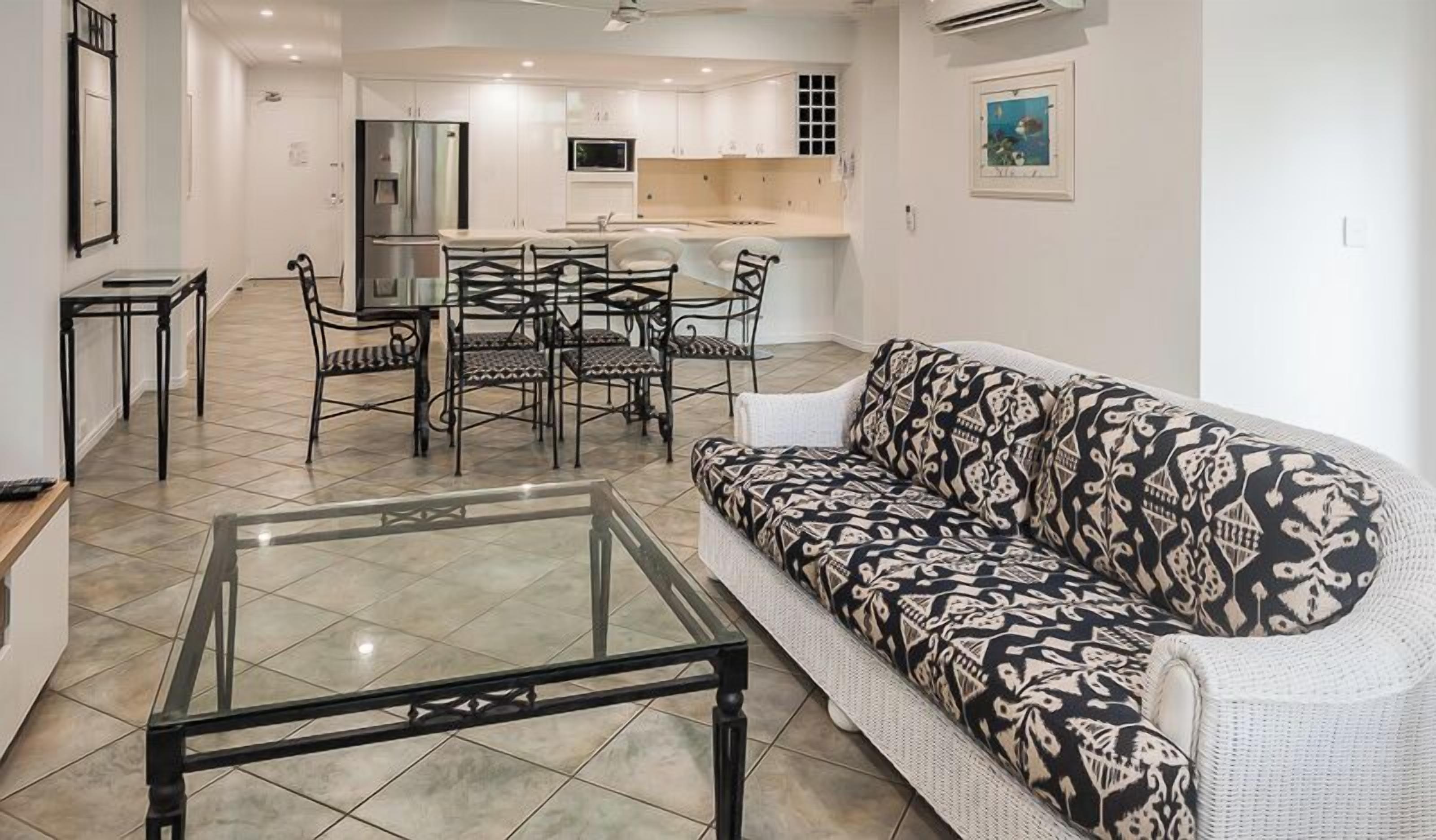 Una sala de estar moderna con una mesa de centro de vidrio, un sofá estampado y un comedor con mesa y sillas.