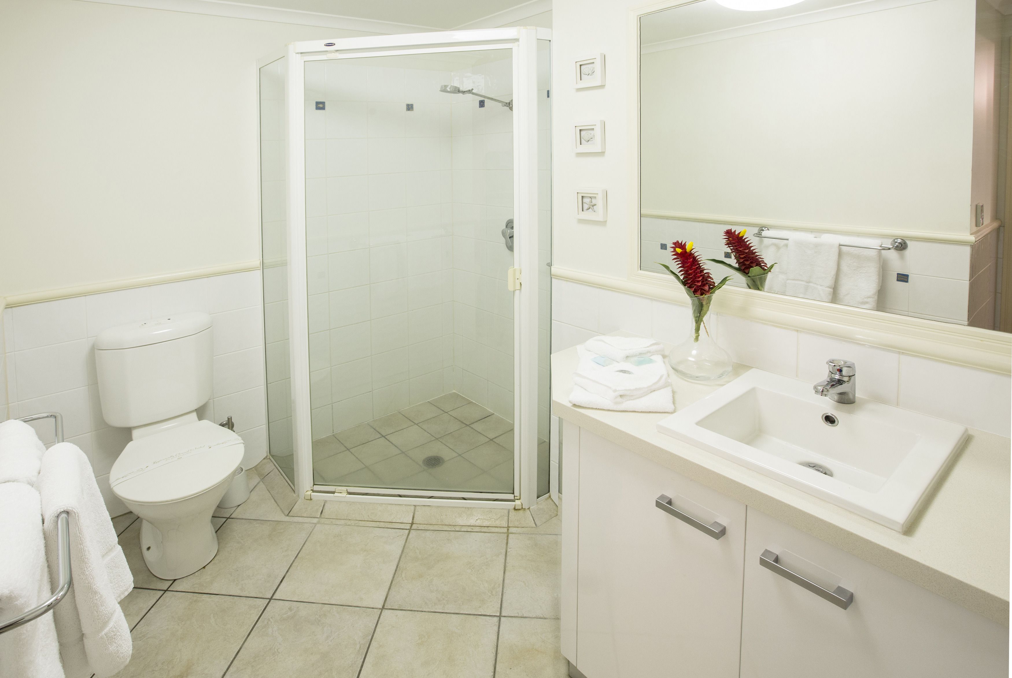 A bathroom with a toilet, shower, sink, and mirror.