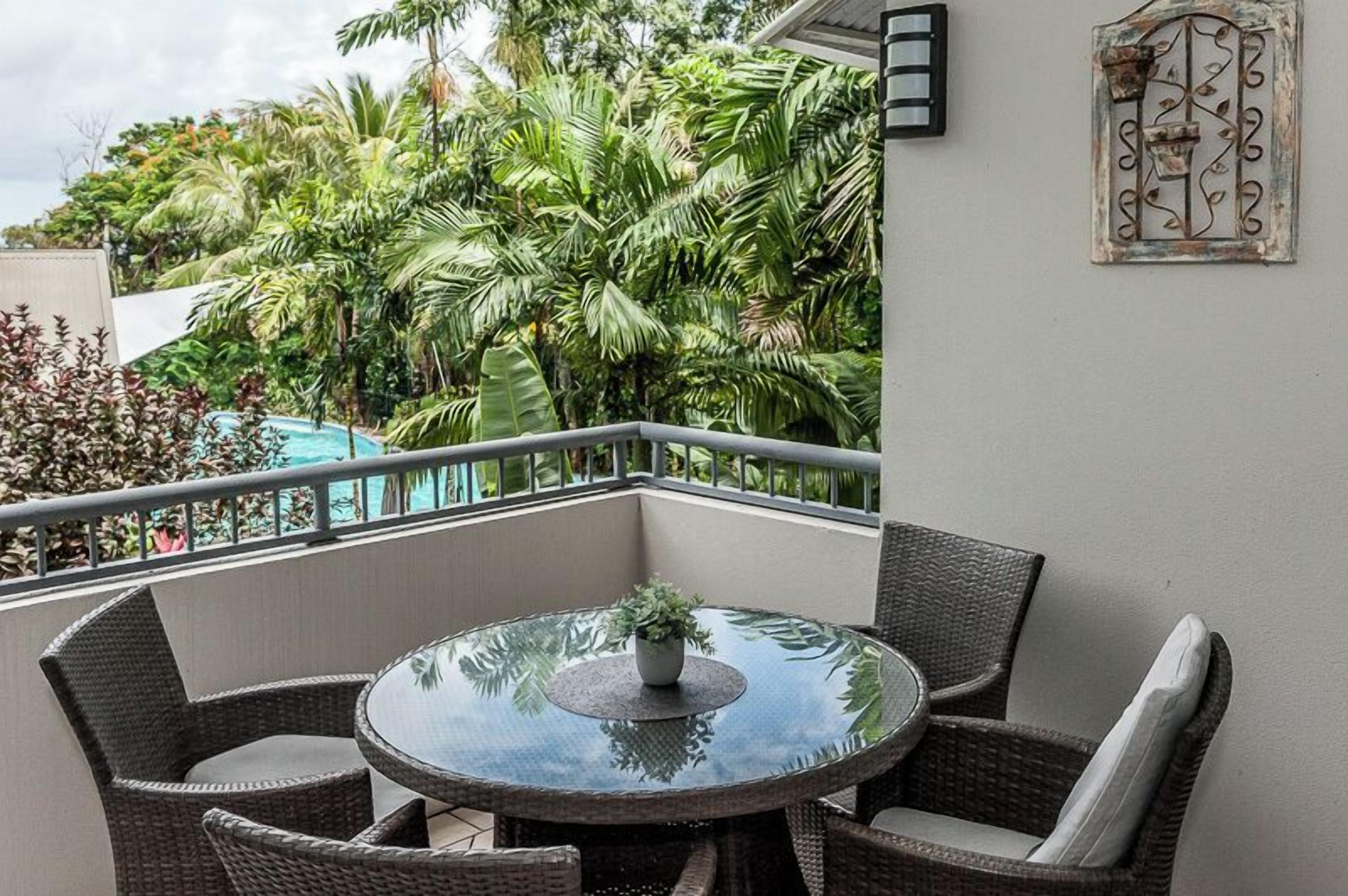 A balcony with wicker furniture, a glass table, and a potted plant.