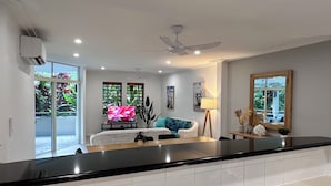 A modern kitchen with a black countertop, stainless steel sink, and a sliding glass door leading to a balcony with a view of greenery. - Oasis at Palm Cove (Palm Cove)