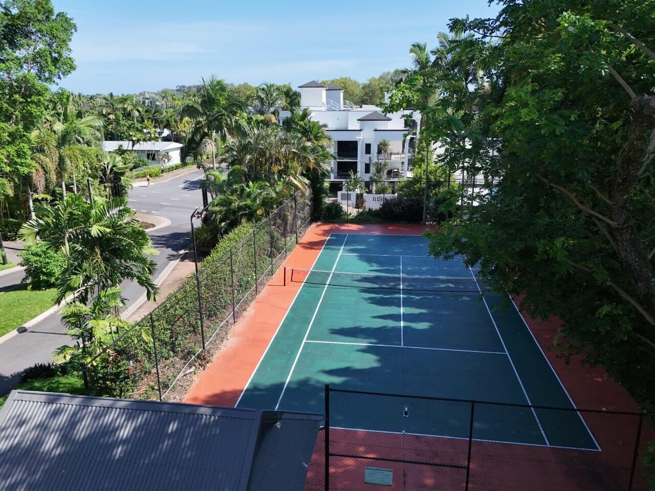 A tennis court surrounded by lush greenery and a modern building in the background.