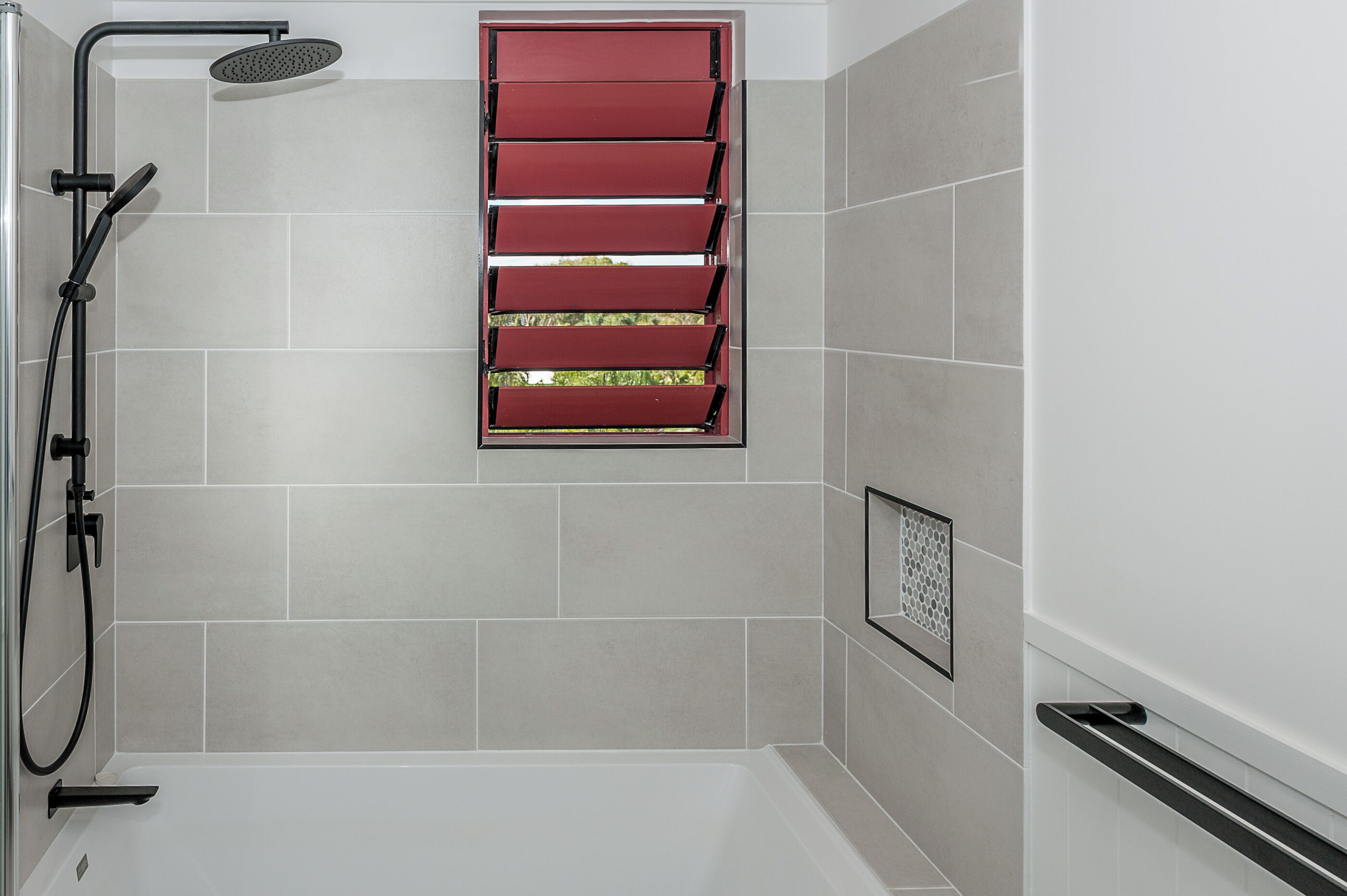 A modern bathroom with a shower, a red window, and a white bathtub.