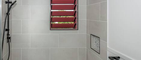 A modern bathroom with a shower, a red window, and a white bathtub.