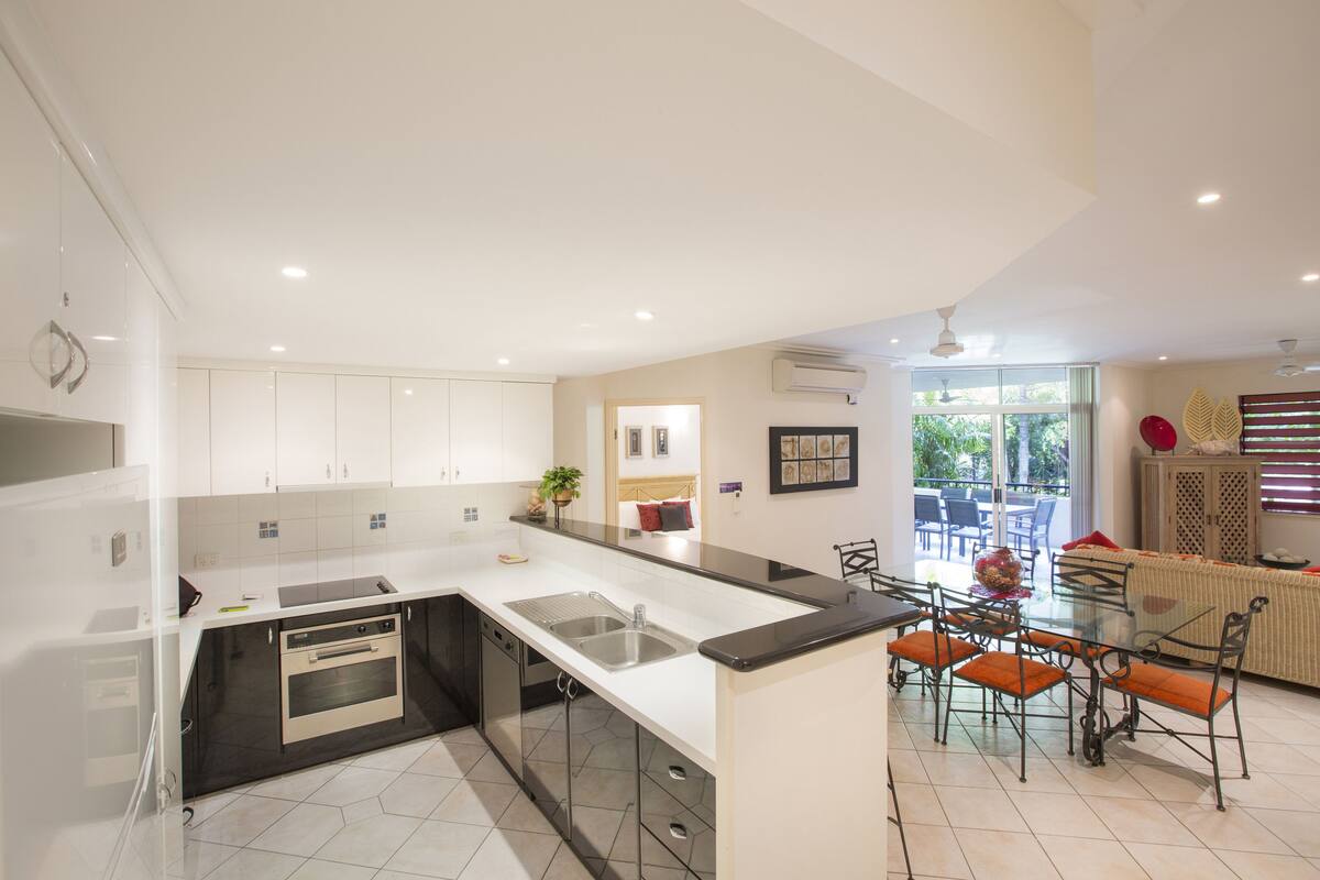 A modern kitchen with a central island, built-in oven, and a dining area with a glass table and chairs.