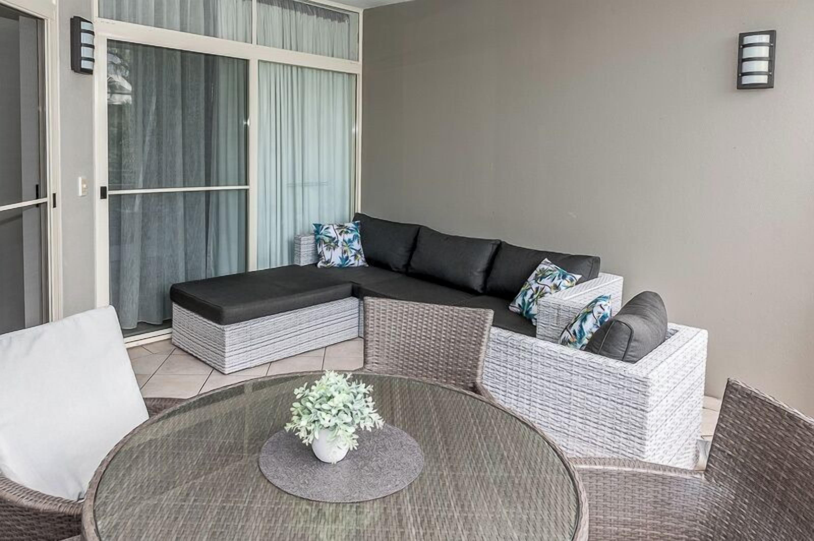 A modern outdoor seating area with a sectional sofa, wicker chairs, and a round table with a plant.