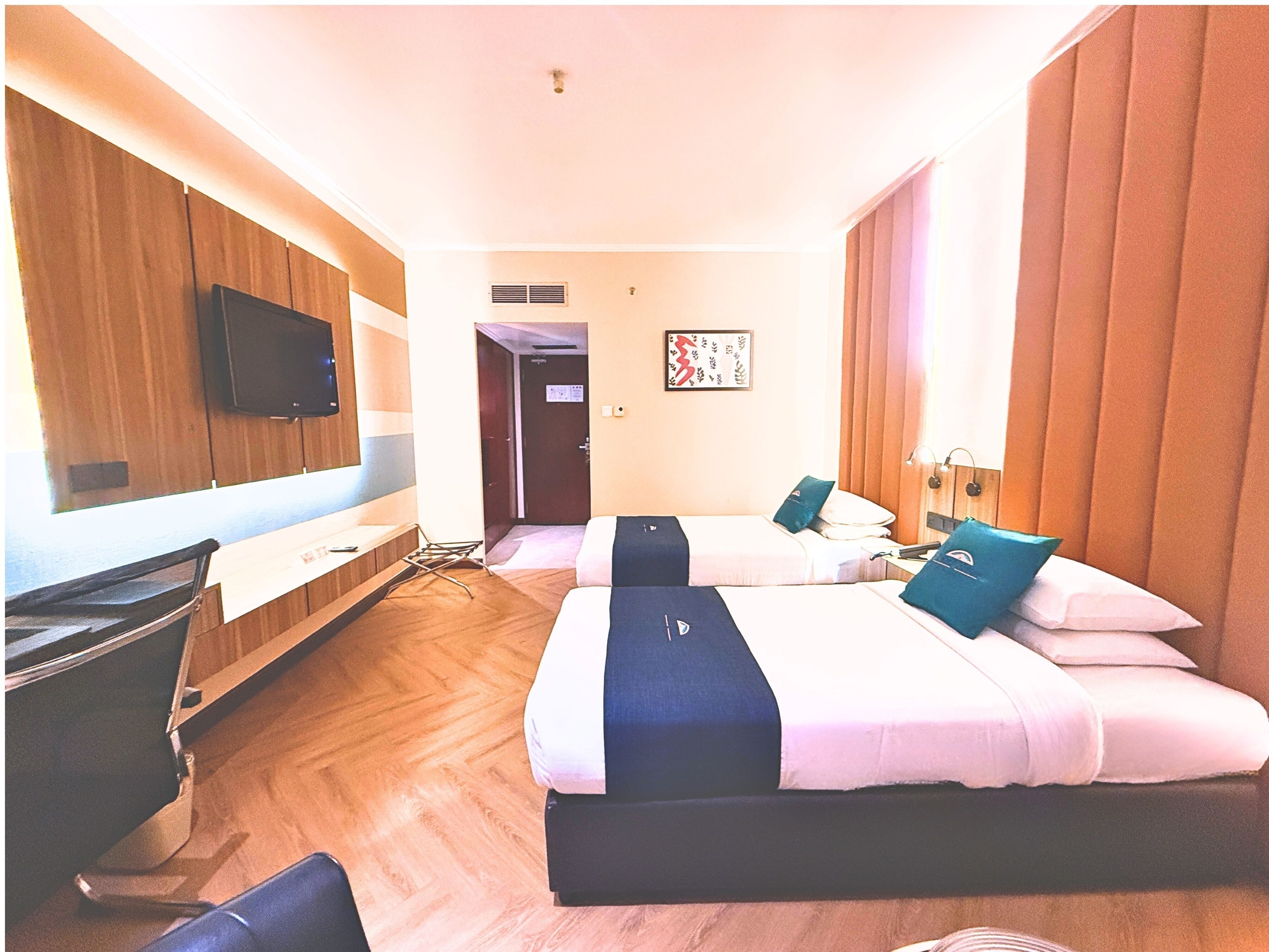 A hotel room with two beds, a flat-screen TV mounted on the wall, a desk, and a chair.