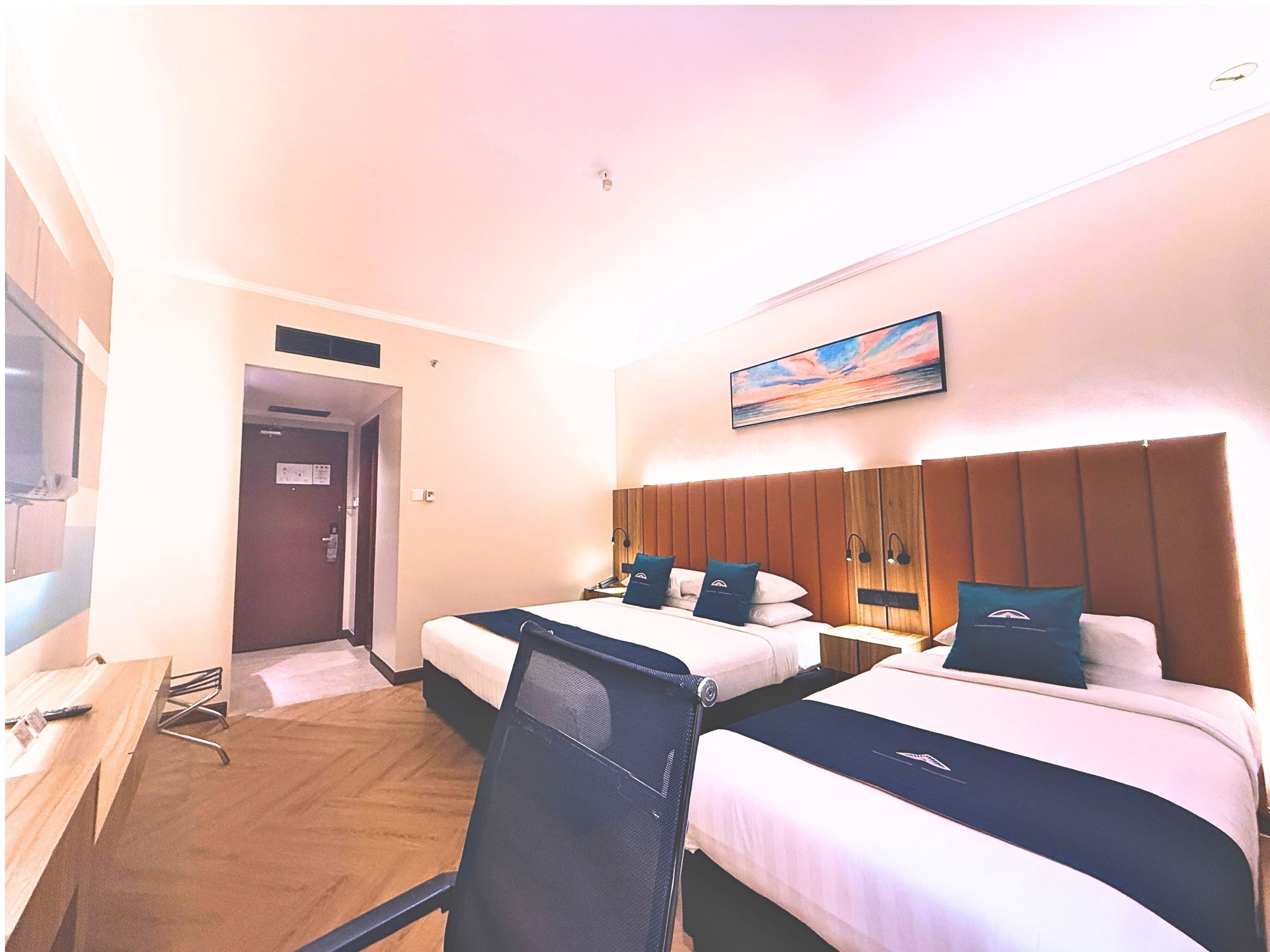 A hotel room with two beds, a desk, and a TV.