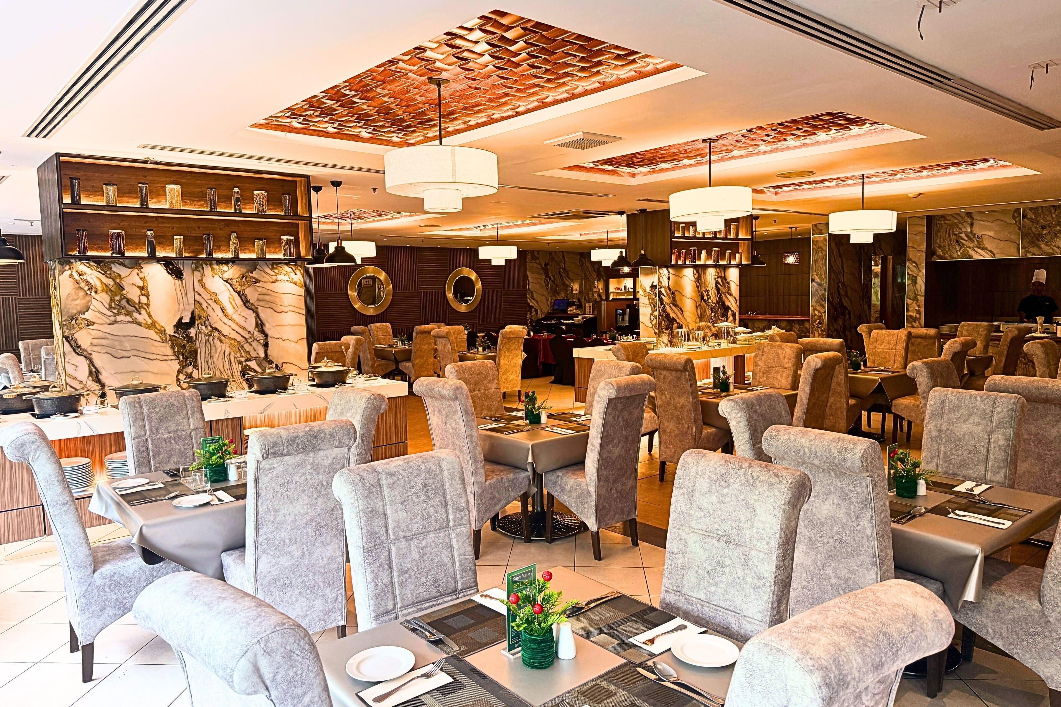 A restaurant with multiple dining tables, grey upholstered chairs, and a marble accent wall.