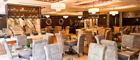 A restaurant with multiple dining tables, grey upholstered chairs, and a marble accent wall.