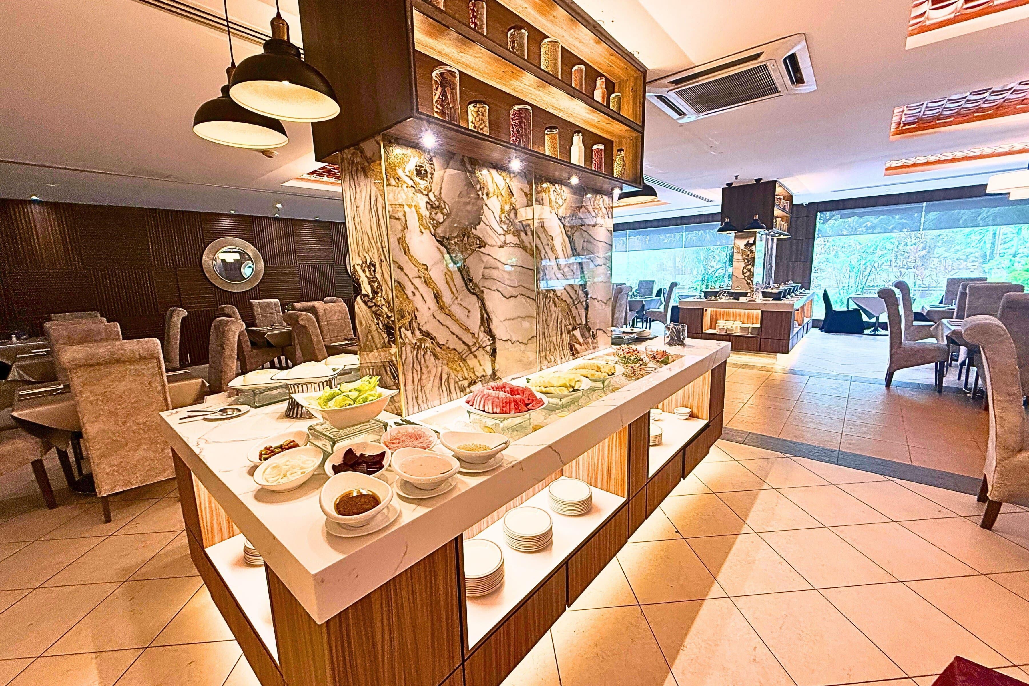 Un buffet proposant une variété de plats, un mur décoratif en marbre et un espace détente avec des chaises et des tables.