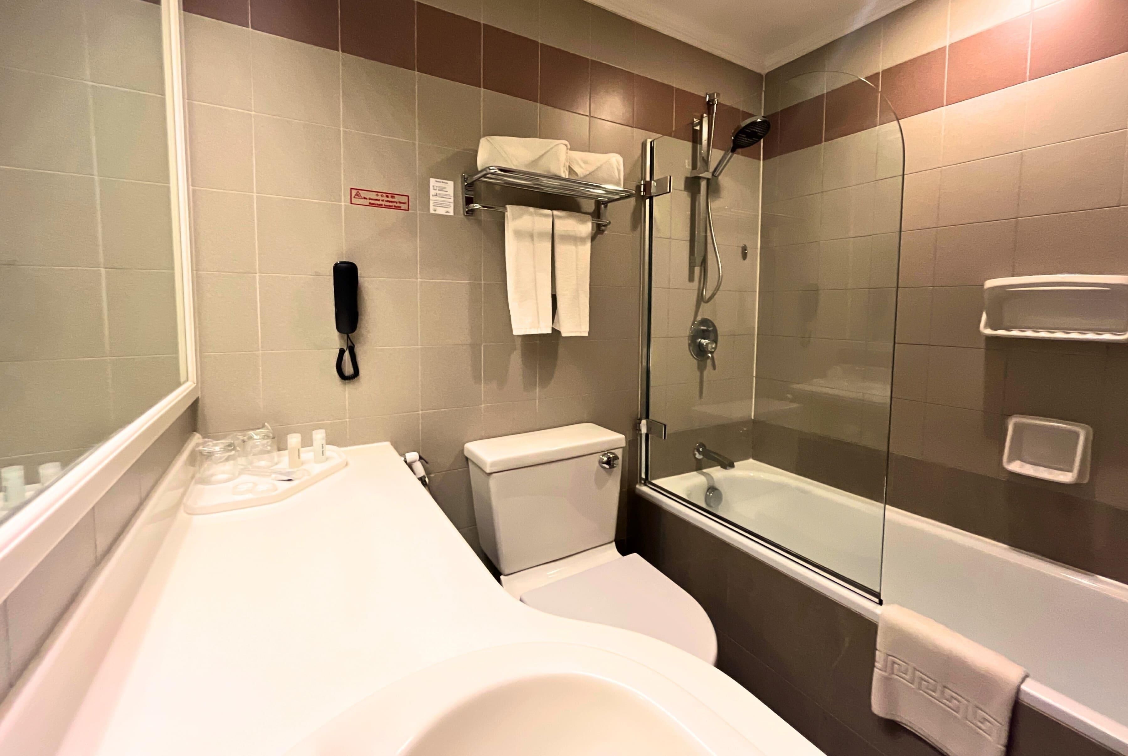 A bathroom with a toilet, a shower, a glass-enclosed bathtub, a towel rack, and a telephone.
