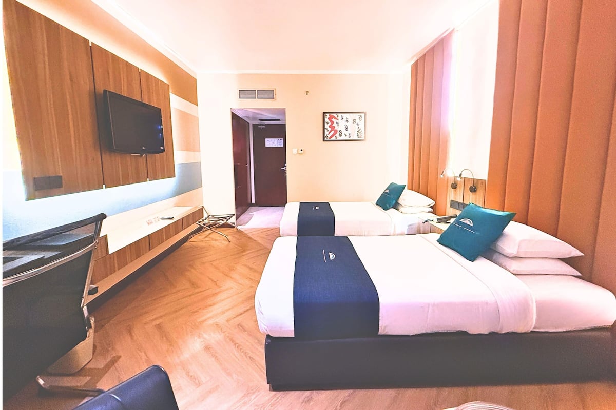A hotel room with two beds, a desk, a television, and a door leading to another room.