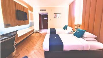 Una habitación de hotel con dos camas, un escritorio, un televisor y una puerta que da a otra habitación.