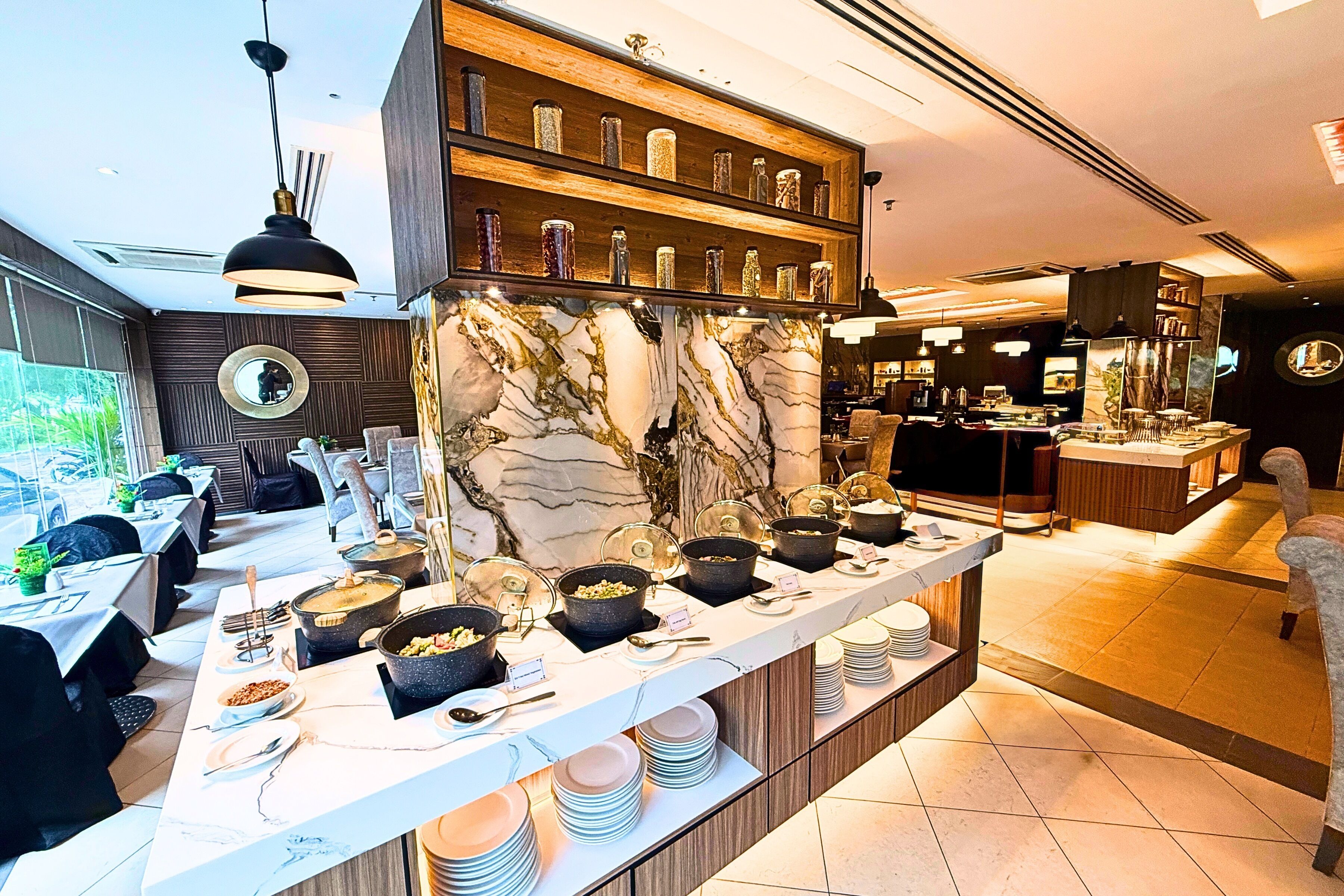 A modern restaurant with a marble bar, dining tables, and a variety of dishes displayed on the counter.