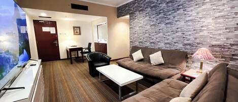 Habitación de hotel moderna con un televisor de pantalla plana grande, un sofá marrón, una mesa de centro blanca y una pared con diseño.