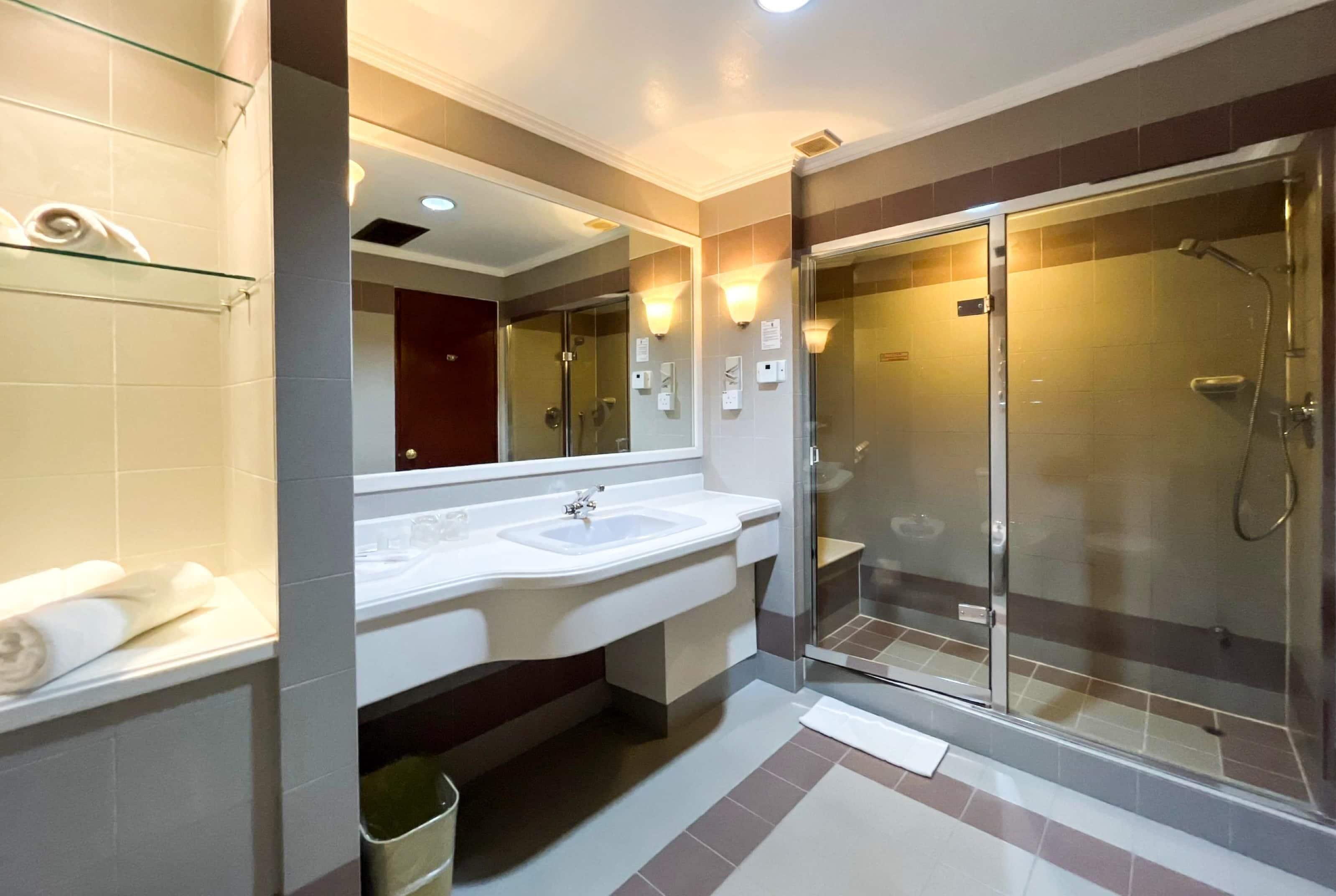 A modern bathroom with a glass-enclosed shower, a large mirror, and a white sink.