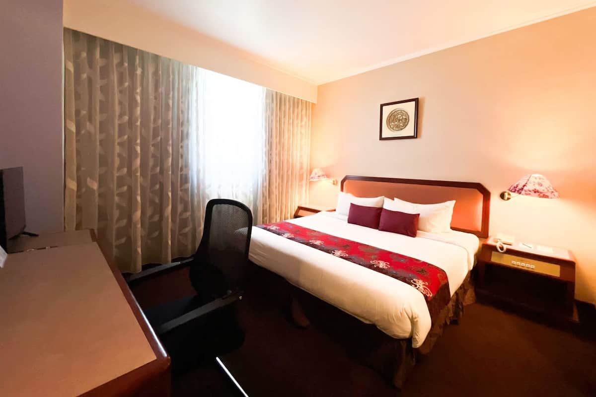 A hotel room with a bed, desk, chair, lamps, and a framed picture on the wall.