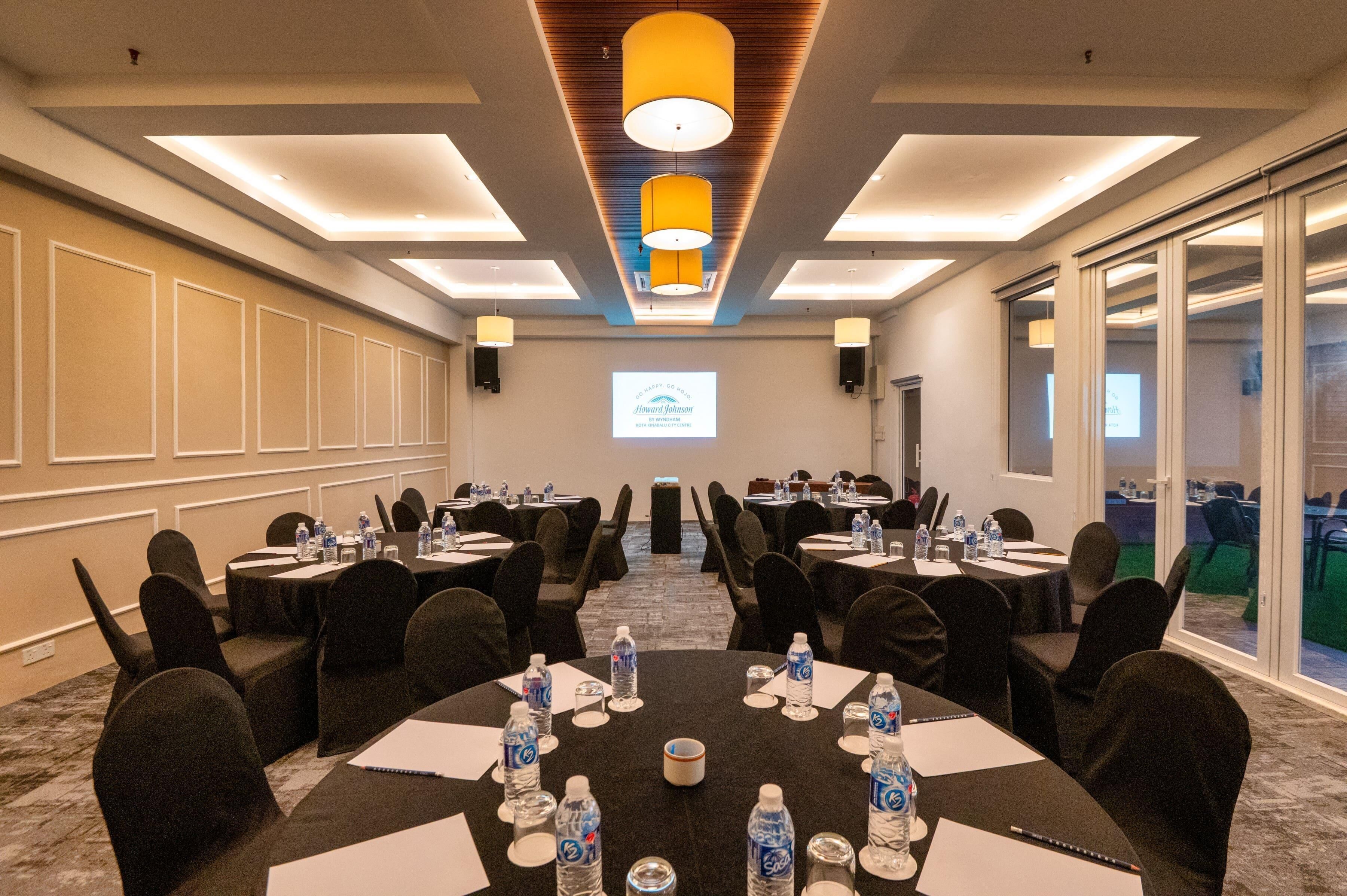 A conference room with tables, chairs, water bottles, and a projector screen.