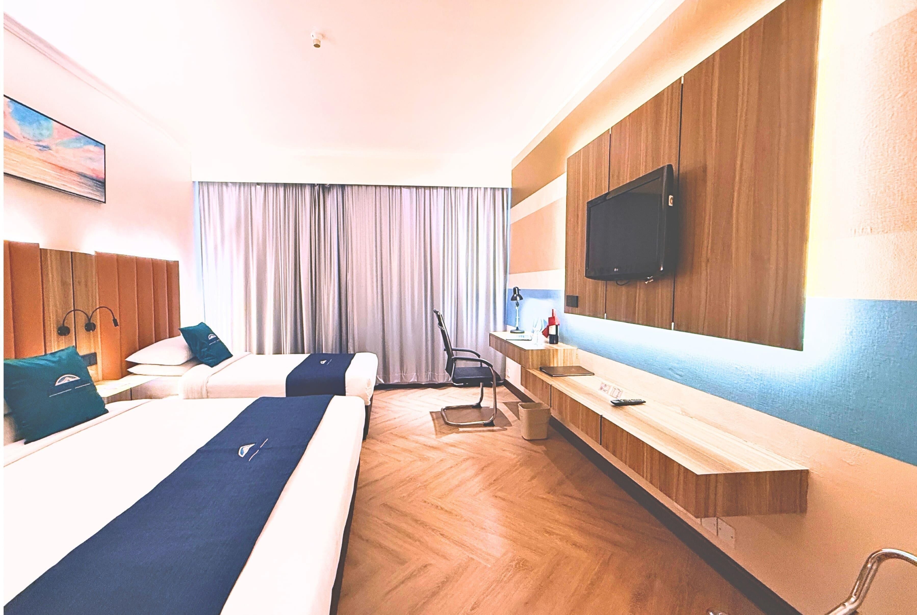 Une chambre d’hôtel avec deux lits, un bureau, une chaise, une télévision et une fenêtre avec des rideaux.