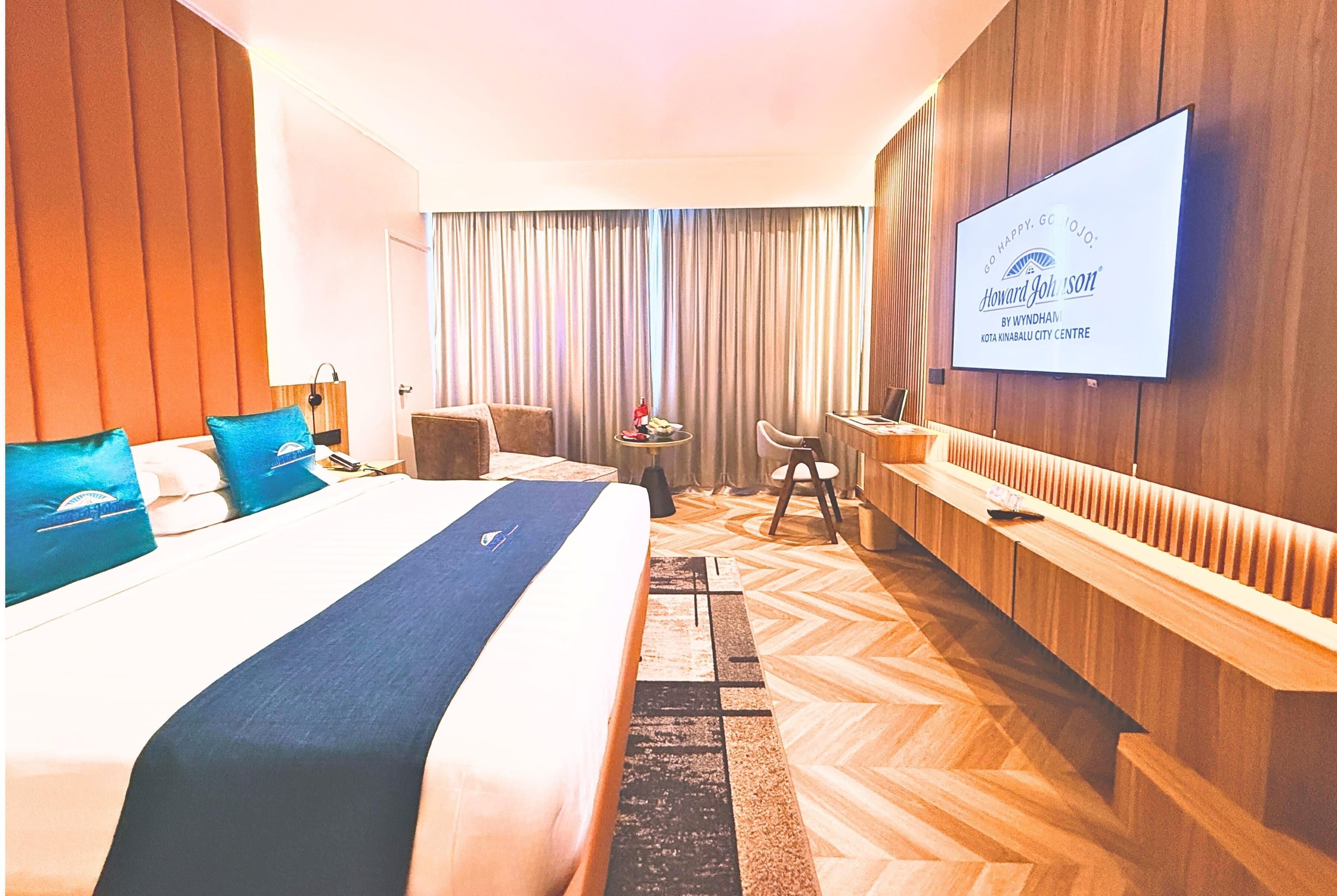 A hotel room with a large bed, a TV mounted on the wall, a desk, and a chair.