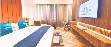 A hotel room with a large bed, a TV mounted on the wall, a desk, and a chair.