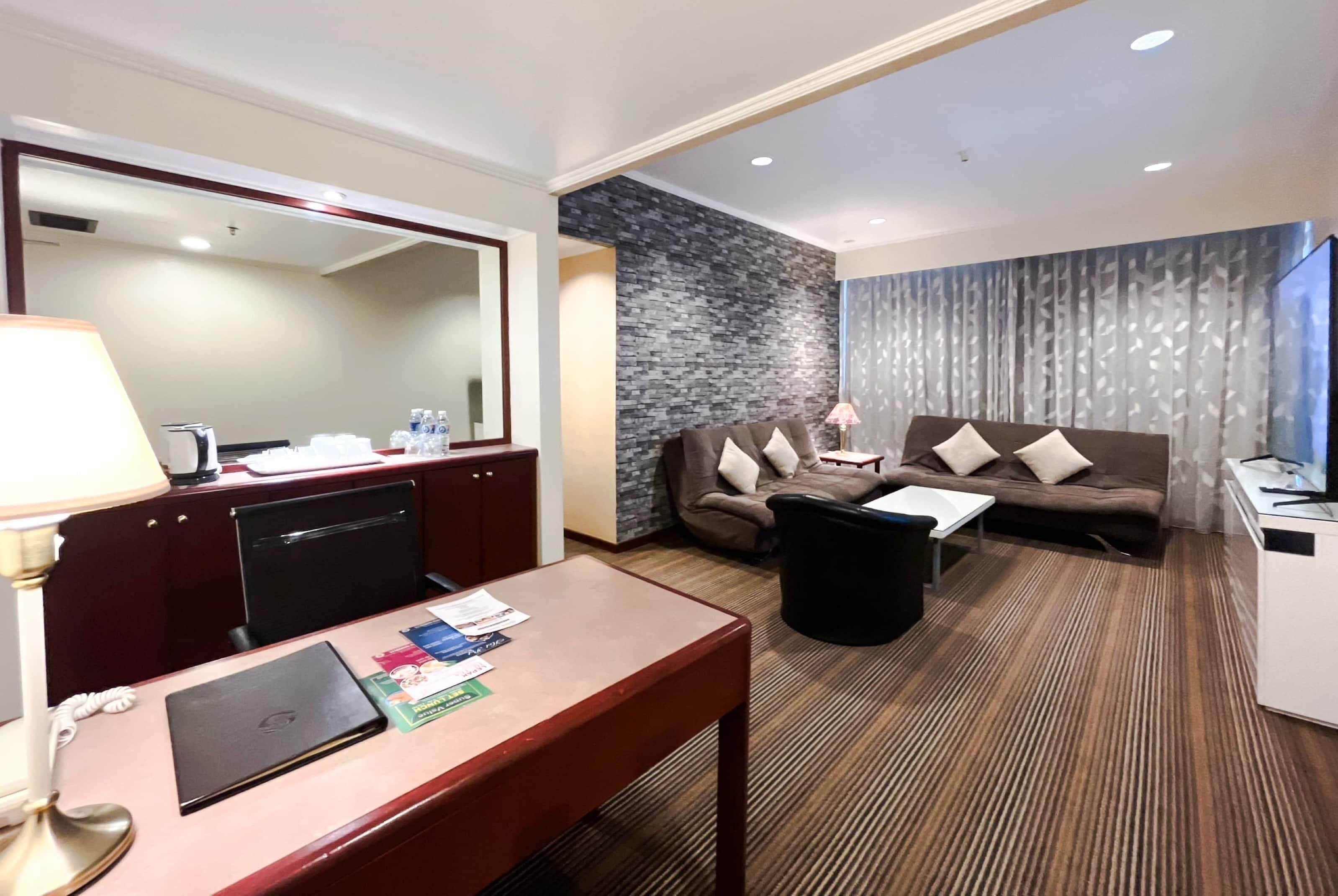 Une chambre d’hôtel équipée d’un bureau, d’un canapé, d’une télévision, d’un miroir et d’un mur décoratif en pierre.