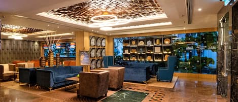 Eine moderne Lobby mit Sitzgelegenheiten, einer Wand mit gerahmten Objekten und einer dekorativen Decke.