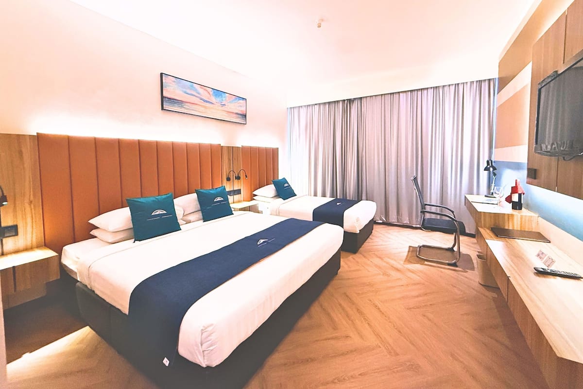 A hotel room with two beds, a desk, a chair, a TV, and a painting on the wall.