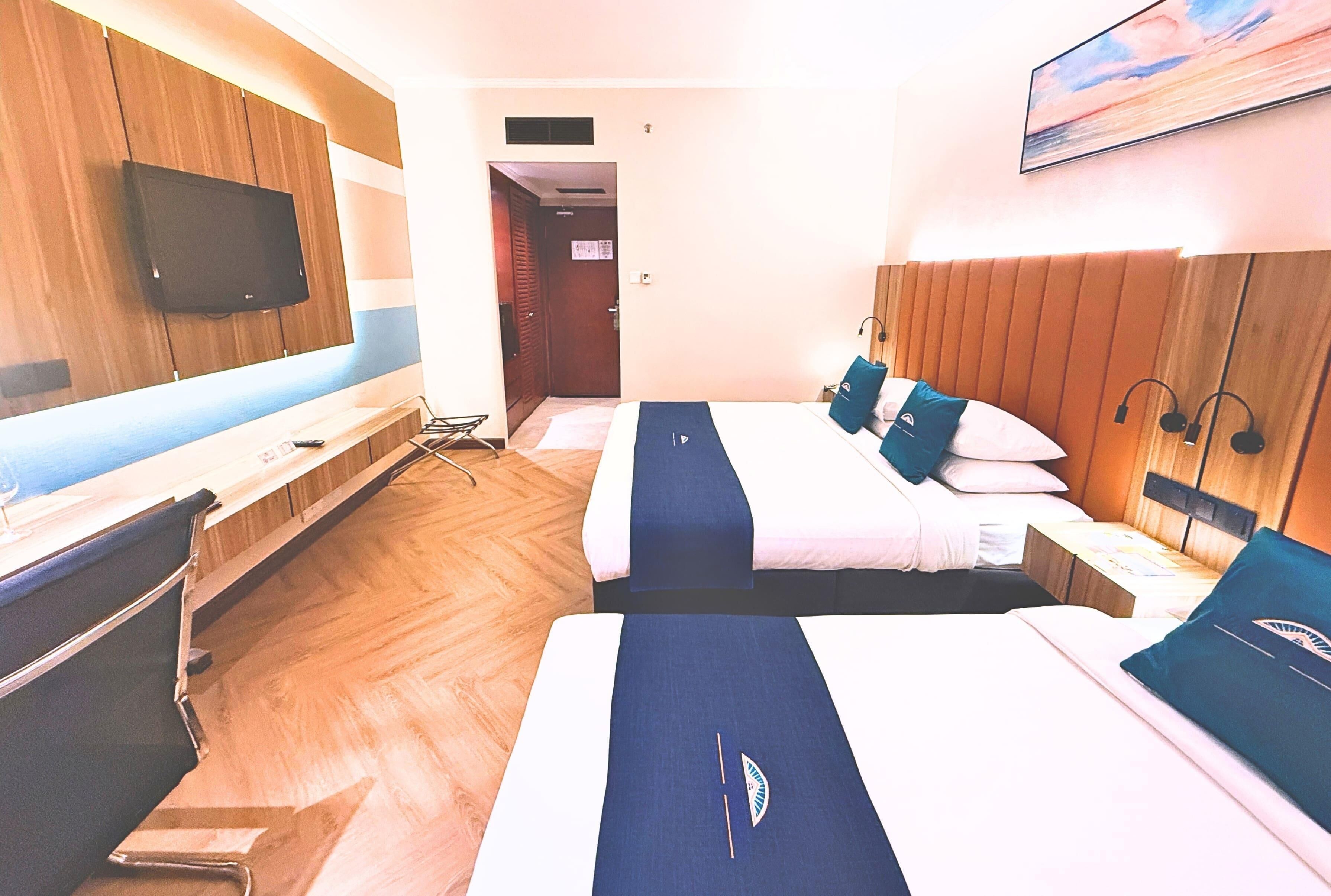 Una habitación de hotel con dos camas, un televisor montado en la pared y suelo de madera.