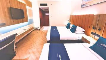 A hotel room with two beds, a TV mounted on the wall, and a wooden floor.