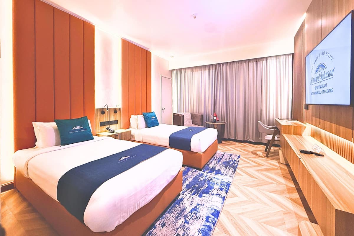 A hotel room with two beds, a desk, a TV, and a large window with curtains.