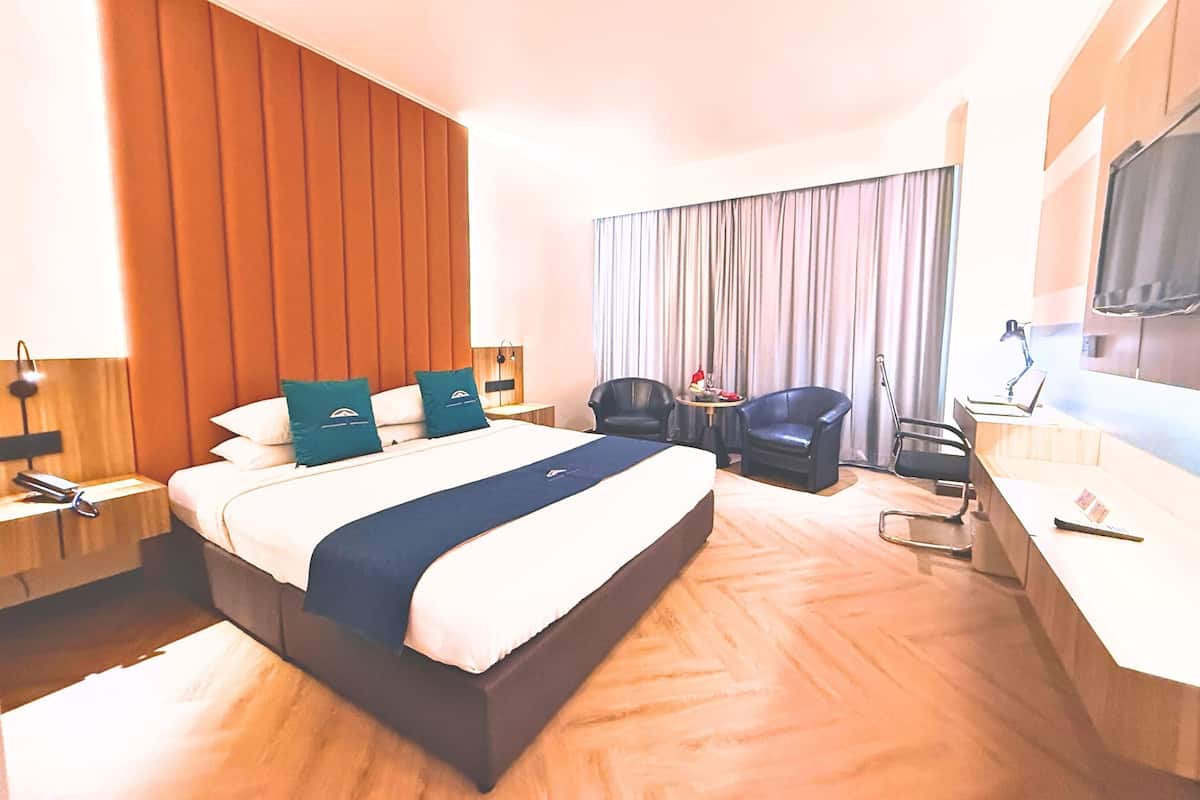 A hotel room with a bed, two chairs, a desk, a TV, and a curtain.