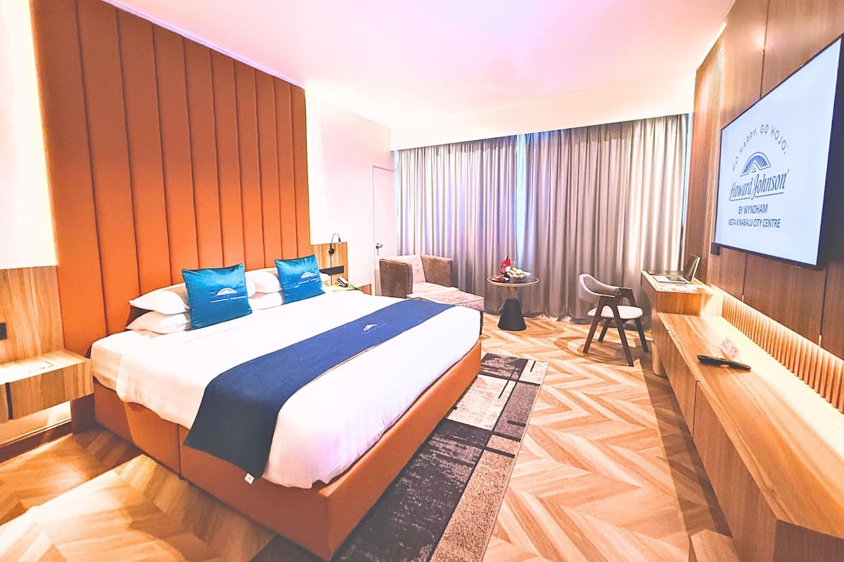 A hotel room with a large bed, a desk, a chair, a TV, and a view of the city center.
