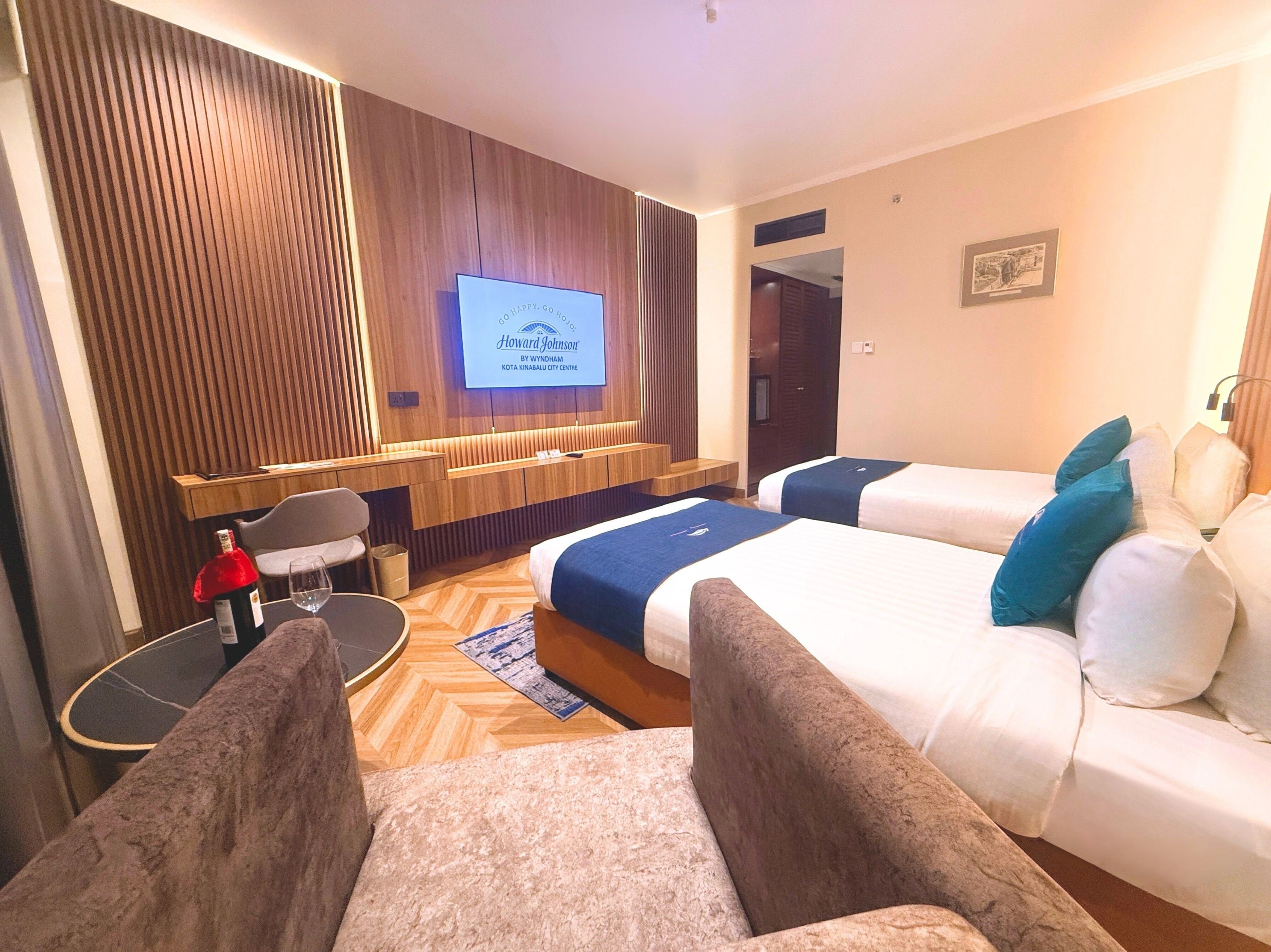A hotel room with two beds, a desk, a chair, a TV screen, and a wooden panel wall.